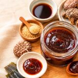 干し椎茸・昆布・醤油・きび砂糖などの材料と一緒に並べた、手作りの植物性オイスターソースの小瓶を真上から撮影した写真