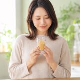 アリサンのニュートリショナルイースト200gの粉末入り瓶を両手で胸の前に持ち、ナチュラルキッチンを背景に優しく微笑む35歳の日本人女性。B12補給に役立つ栄養酵母の1年使用レビュー記事サムネイル