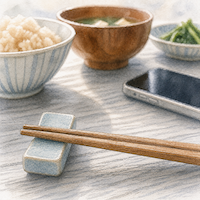 ヴィーガンダイエットの記録で、食べる前に一度立ち止まる瞬間。箸置きに揃えたままの箸と、奥にぼやける料理とスマートフォンを接写した水彩イラスト