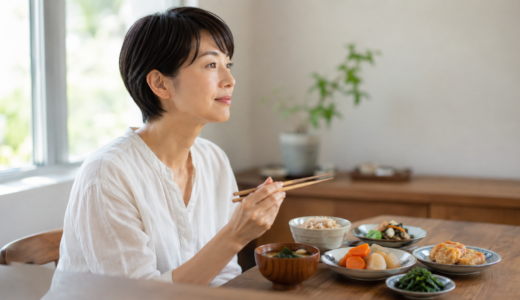 40代からの女性に足りていない栄養。明るいダイニングで、玄米や青菜、にんじん、わかめの汁ものなど品数の多い食事を前に、女性が箸を止めて考えている