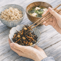 ヴィーガンダイエットで血糖値がゆるやかになる食物繊維の多い食事。ひじきと大豆の小鉢を箸で持ち上げ、玄米ごはんと具だくさんの味噌汁を添えた手元の水彩イラスト
