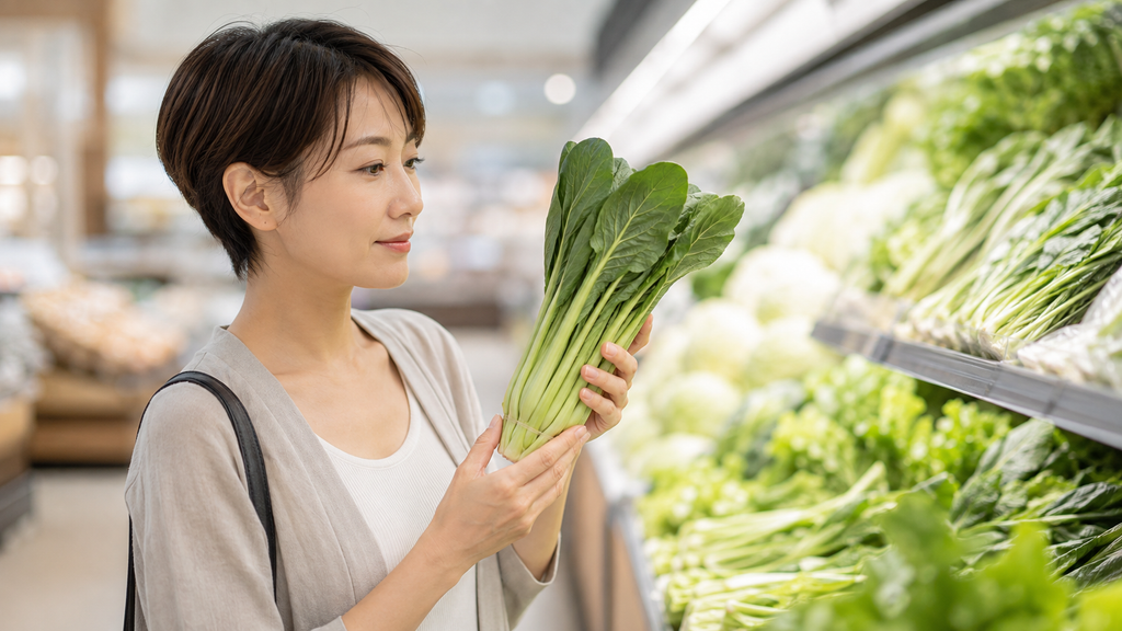 スーパーの野菜売り場で小松菜を手に取る女性。カルシウムと鉄は甘酒ではなく食事から摂る