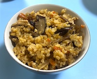天日で干した干ししいたけと戻し汁で炊いた玄米の炊き込みご飯。切った干ししいたけとにんじん、ごぼう、千切り大根、昆布が茶碗によそわれている
