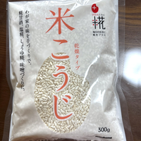 甘酒の材料に使っている乾燥タイプの米こうじ300gの袋。木のテーブルに置いて真上から見たところで、我が家が5年使っているもの