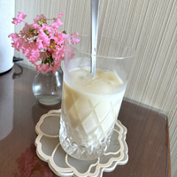 豆乳で割った甘酒を氷とマドラーごと背の高いグラスに注ぎ、サルスベリの花を生けた花瓶のそばに置いたところ。疲れが残った日に飲む一杯