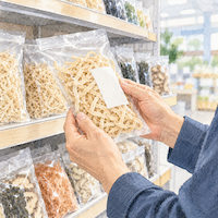 切り干し大根は袋の産地を見て買う。乾物の棚の前で切り干し大根の袋を手に取り、裏の表示を確かめる手元の水彩イラスト