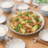 ヴィーガンと家族の食事で同じ一皿を囲む。食卓の真ん中に、豚肉と見分けのつかない大豆ミートの回鍋肉の大皿があり、3人分の取り皿とごはんが並ぶ水彩イラスト