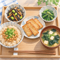 テンペ1袋で1日にとりたい食物繊維の半分以上がとれる。焼いたテンペ、納豆ごはん、わかめのみそ汁、野菜のおかずが並ぶ朝ごはんの水彩イラスト